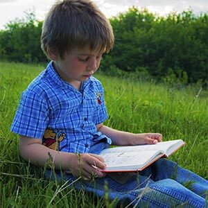 boy sitting in grass and reading a book